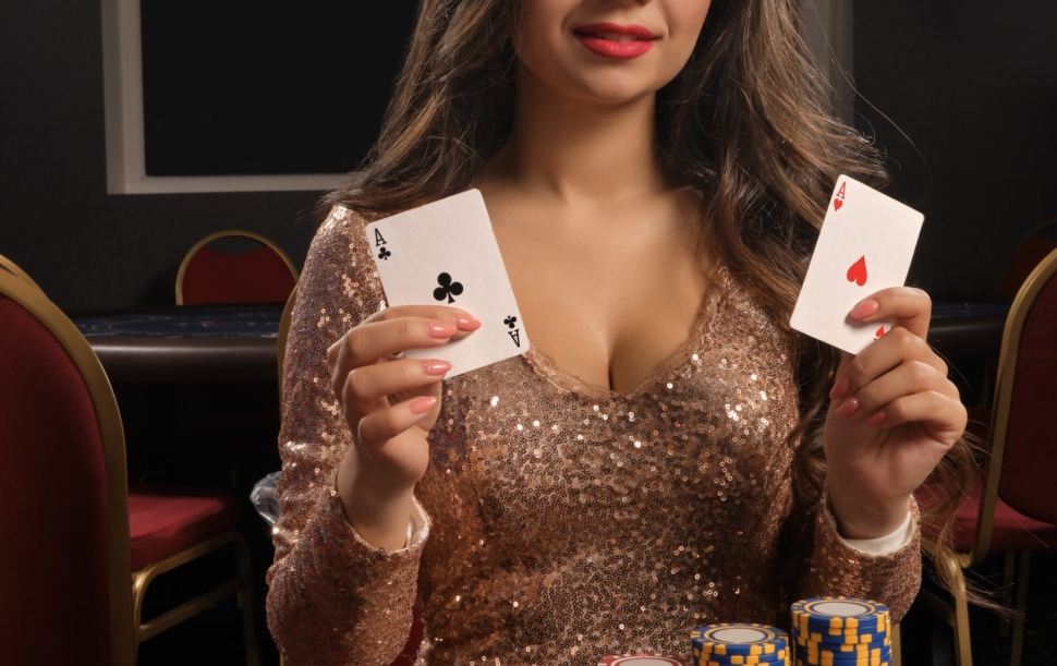 Beautiful brunette woman in a brilliant gold dress is playing poker sitting at the table in casino. She is making bets waiting for a big win and showing her cards. Gambling for money. Games of fortune.